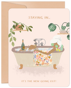 Front view of a light pink greeting card for her, featuring a woman with white hair relaxing in a bubble bath with cucumber slices on her eyes, champagne, and houseplants. Text reads 'STAYING IN... IT'S THE NEW GOING OUT!'