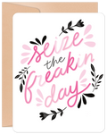 Encouraging greeting card for a friend, featuring vibrant pink script 'Seize the freakin' day' on a white background with decorative black and pink floral accents. Includes a brown envelope.