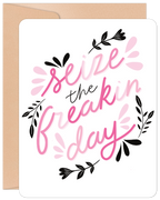 Encouraging greeting card for a friend, featuring vibrant pink script 'Seize the freakin' day' on a white background with decorative black and pink floral accents. Includes a brown envelope.