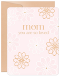 Heartfelt floral birthday card for Mom featuring 'Mom you are so loved' text in elegant gold, delicate white and gold outline flowers on a soft pink background, with a natural kraft envelope. Perfect for celebrating a mother's special day.
