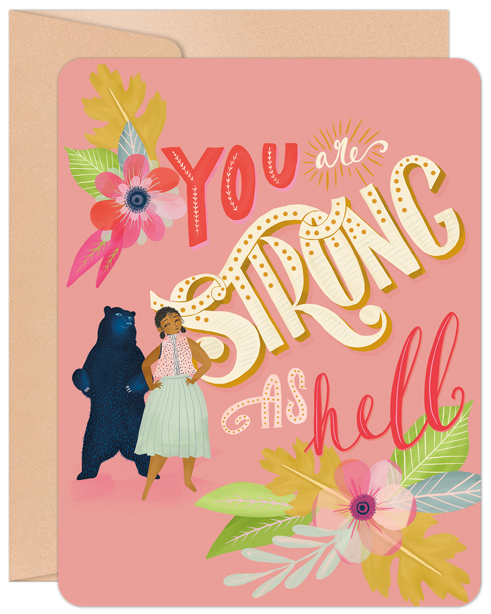 Front of a pink greeting card featuring a woman and a bear with colorful floral accents. Text: "YOU are STRONG AS hell".