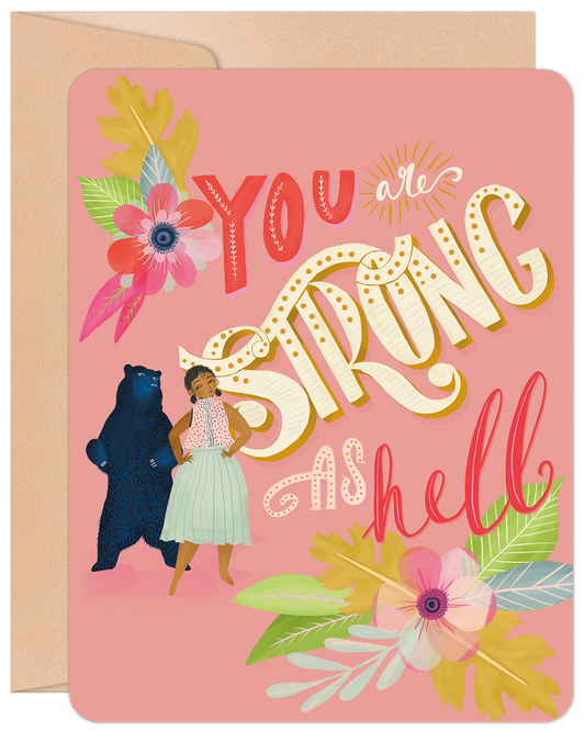 Front of a pink greeting card featuring a woman and a bear with colorful floral accents. Text: "YOU are STRONG AS hell".