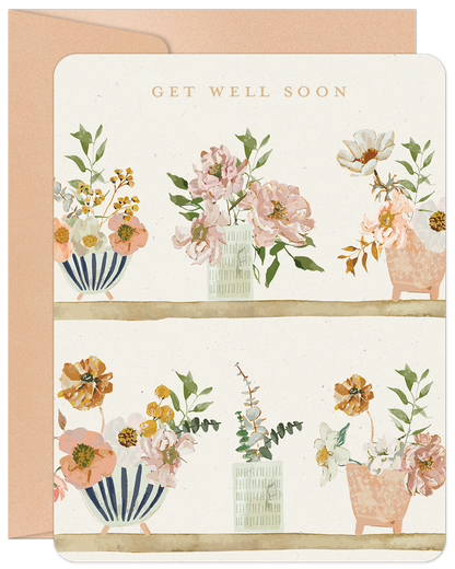 Get Well Soon card featuring watercolor floral arrangements in various vases on two rustic shelves, with a soft peach envelope.