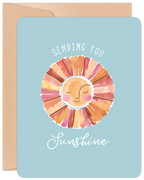 Front of a light blue get well greeting card featuring a cheerful watercolor sun illustration and the text 'SENDING YOU Sunshine' in white script, paired with a kraft envelope.