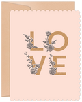 Close-up of a light pink scalloped greeting card with 'LOVE' in gold glitter texture, adorned with intricate black and white floral illustrations. A kraft envelope is visible behind.