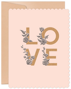 Close-up of a light pink scalloped greeting card with 'LOVE' in gold glitter texture, adorned with intricate black and white floral illustrations. A kraft envelope is visible behind.