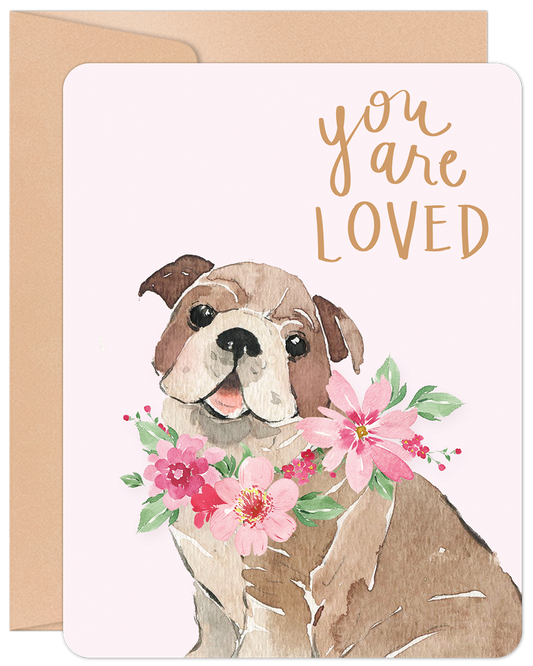 Front of a 'You Are Loved' greeting card with a watercolor bulldog wearing pink flowers and gold text on a light pink background.