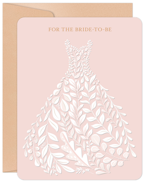 Elegant pale pink greeting card featuring a white intricate floral design forming a wedding dress silhouette, with gold text 'FOR THE BRIDE-TO-BE'. Includes a brown kraft envelope.