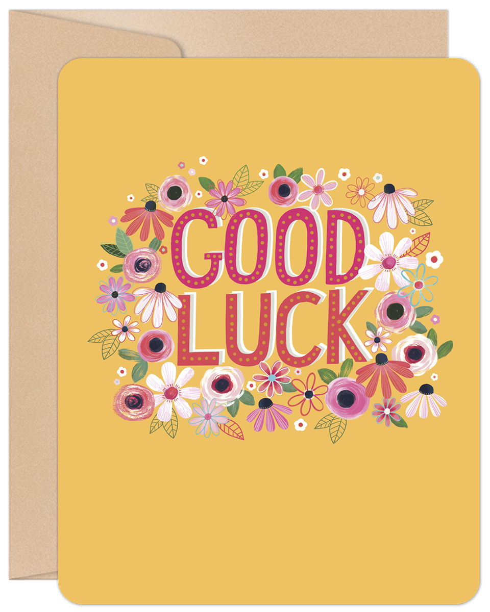 Vibrant yellow greeting card with 'GOOD LUCK' in pink letters, surrounded by a cheerful wreath of colorful flowers, with a brown envelope peeking behind.