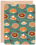 Front of a festive greeting card featuring a charming pattern of various holiday pies, including pumpkin, apple, and pecan, decorated with whipped cream, berries, cinnamon sticks, and nuts on a teal background. The text 'Happy Thanksgiving' is visible.