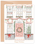 Close-up of a festive holiday greeting card featuring an illustrated white house with a pink door, adorned with green garlands, red bows, string lights, and wreaths, all against a kraft paper envelope.