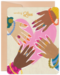 Front of a heartfelt encouragement greeting card featuring diverse hands adorned with jewelry, forming a pink heart. The text 'sending Love' is visible. A kraft envelope is partially seen behind it. Ideal for a friend needing support.