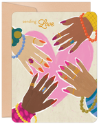 Front of a heartfelt encouragement greeting card featuring diverse hands adorned with jewelry, forming a pink heart. The text 'sending Love' is visible. A kraft envelope is partially seen behind it. Ideal for a friend needing support.