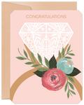 Elegant engagement greeting card featuring a large white lace diamond ring illustration with vibrant pink and teal floral accents and green leaves on a soft pink background. Gold 'CONGRATULATIONS' text is at the top, presented with a kraft envelope.