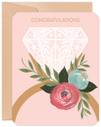 Elegant engagement greeting card featuring a large white lace diamond ring illustration with vibrant pink and teal floral accents and green leaves on a soft pink background. Gold 'CONGRATULATIONS' text is at the top, presented with a kraft envelope.