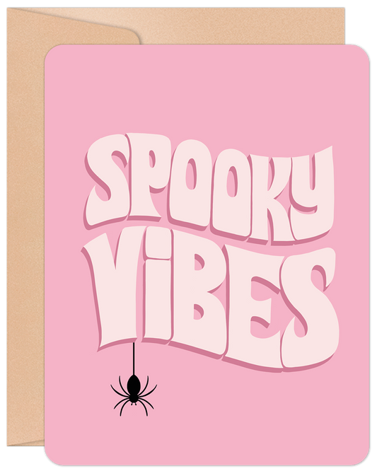 Pink Halloween greeting card featuring "Spooky Vibes" text in white and a black spider, resting on a brown kraft envelope.