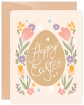 Front of a cute Easter greeting card featuring a central brown egg with 'Happy Easter' in white script, framed by colorful floral elements including pink tulips, yellow and purple flowers, and green leaves. A kraft paper envelope is visible behind the card.