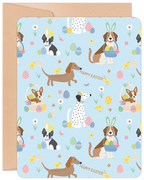 Front of an Easter greeting card featuring a light blue background patterned with various cute cartoon dogs in bunny ears, colorful decorated eggs, and yellow chicks. Dog breeds include Beagle, Boston Terrier, Dachshund, Dalmatian, and Corgi. Text reads "HAPPY EASTER".