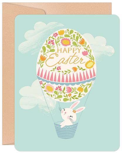 Front of a cute Easter card featuring a bunny in a floral hot air balloon with 'Happy Easter' text on a sky blue background.