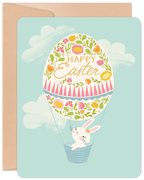 Front of a cute Easter greeting card featuring an adorable white bunny in a hot air balloon shaped like a decorated floral egg, against a light blue sky with white clouds. 'Happy Easter' is written on the egg.