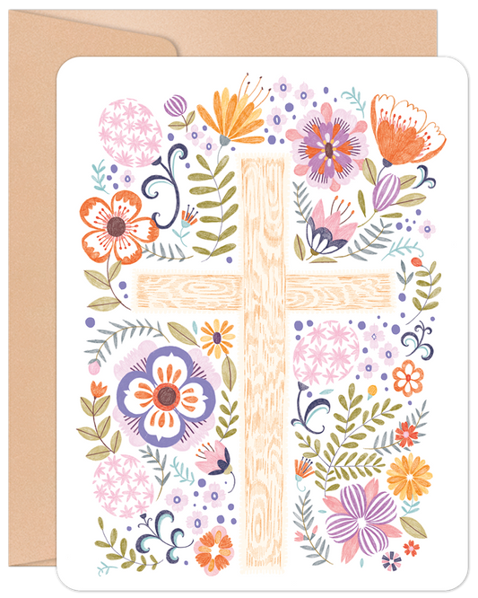 Front of a greeting card featuring a folk-art style wooden cross adorned with an abundance of colorful flowers and greenery.