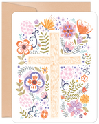 Front of a religious Easter greeting card featuring a wooden cross adorned with a vibrant array of purple, orange, pink, and yellow spring flowers, green leaves, and decorative pastel eggs. A brown kraft envelope is visible in the background, hinting at the high-quality stationery.