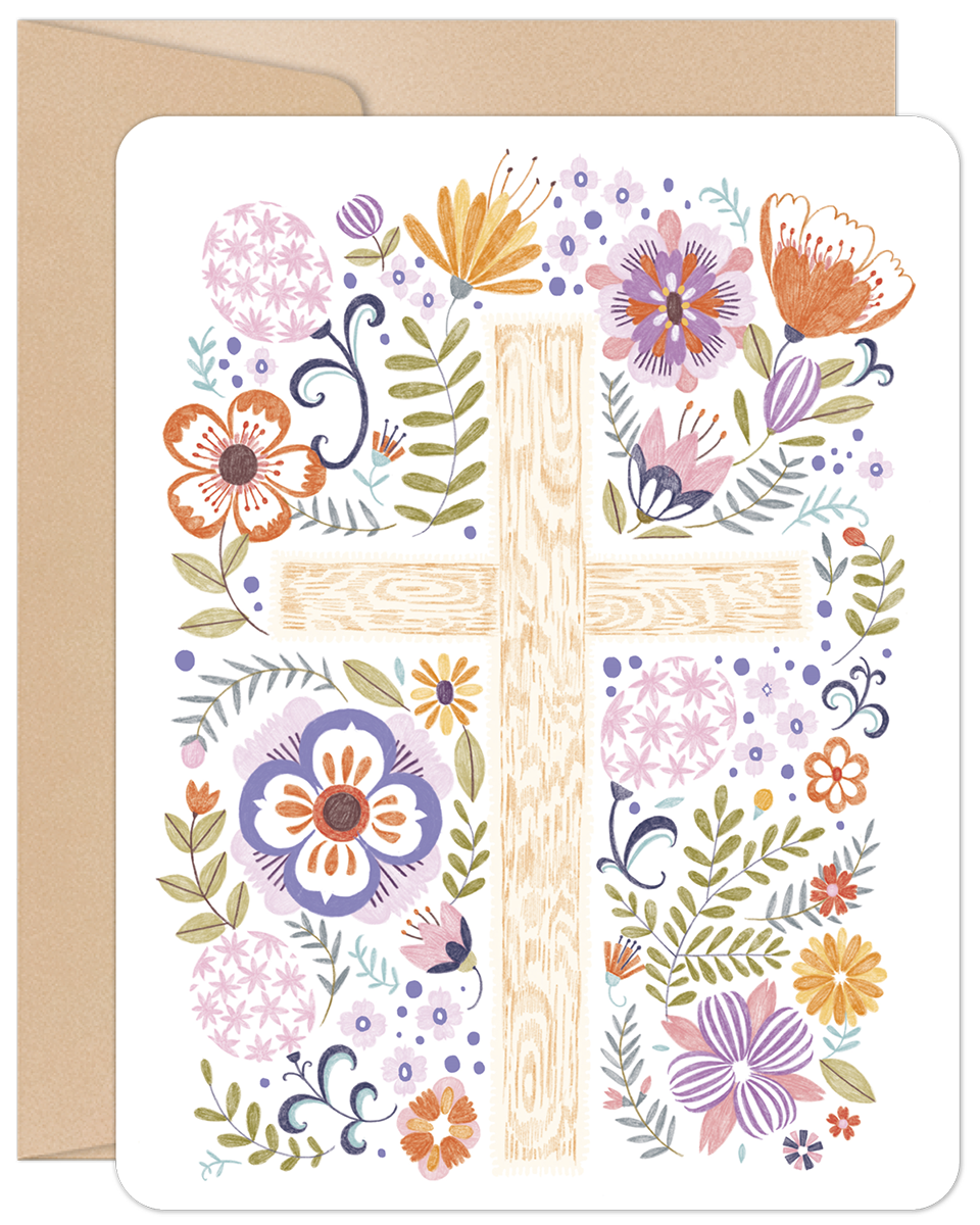 Front of a religious Easter greeting card featuring a wooden cross adorned with a vibrant array of purple, orange, pink, and yellow spring flowers, green leaves, and decorative pastel eggs. A brown kraft envelope is visible in the background, hinting at the high-quality stationery.