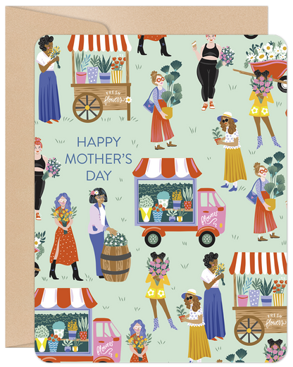 Front of a Happy Mother's Day card with a colorful illustration of women in a bustling flower market scene, presented on a kraft envelope.