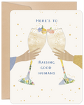 Front view of a cream-colored greeting card featuring two hands holding champagne flutes in a celebratory toast, adorned with delicate floral details and scattered gold stars. The text reads "HERE'S TO RAISING GOOD HUMANS".