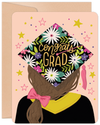 Vibrant floral graduation greeting card featuring an illustrated student in a black cap and gown with 'Congrats Grad' in gold text, surrounded by stars and confetti on a blush pink background, perfect for celebrating a special achievement.