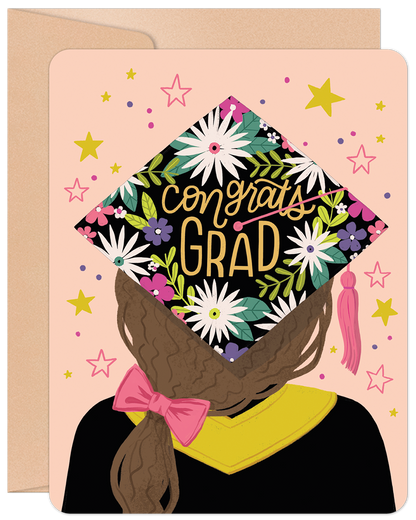 Front of a graduation card featuring a grad girl from behind, wearing a floral 'Congrats Grad' cap, on a pink background with stars.