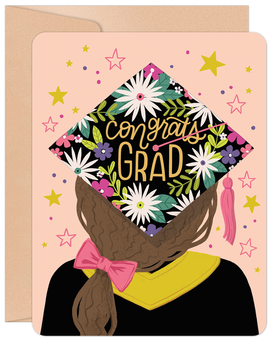 Front of a graduation card featuring a grad girl from behind, wearing a floral 'Congrats Grad' cap, on a pink background with stars.