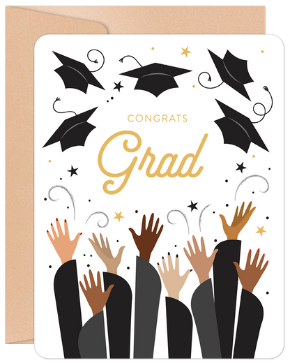 Front of a graduation greeting card showing hands tossing caps, gold 'Congrats Grad' text, and stars on a white background.