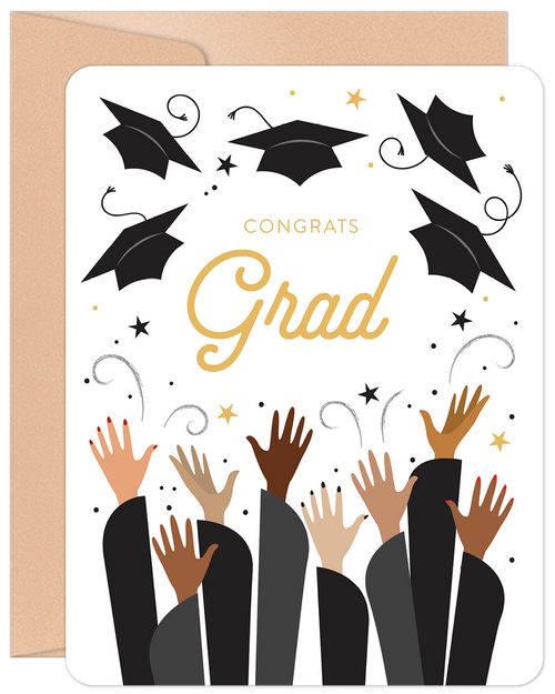 Front of a modern congratulatory card for a graduate, featuring raised hands, black academic caps, gold 'Congrats Grad' text, and scattered gold stars on a white background, accompanied by a kraft envelope.