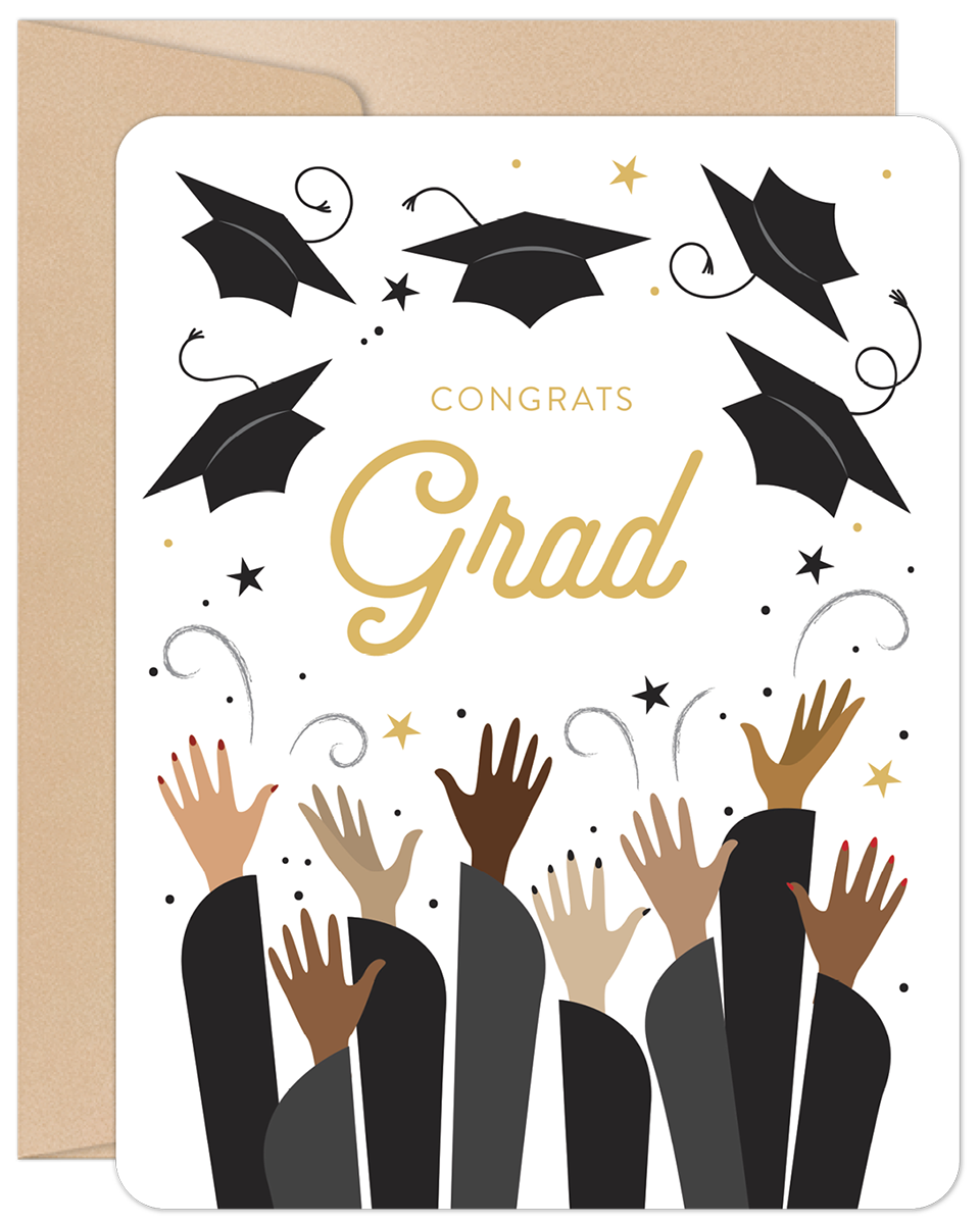 Front of a modern graduation greeting card featuring 'Congrats Grad' in gold typography, surrounded by black tossed graduation caps, gold stars, and diverse hands raised in celebration, set against a white background with a kraft envelope visible.