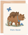 Cute Father's Day greeting card featuring a loving papa bear wearing glasses and a blue bow tie, carrying his small cub on his back. A blue butterfly, green plant, and blue mushroom add to the charming woodland scene. 'PAPA BEAR' text is visible at the bottom. The card is presented with a rustic kraft envelope.