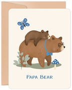 Cute Father's Day greeting card featuring a loving papa bear wearing glasses and a blue bow tie, carrying his small cub on his back. A blue butterfly, green plant, and blue mushroom add to the charming woodland scene. 'PAPA BEAR' text is visible at the bottom. The card is presented with a rustic kraft envelope.