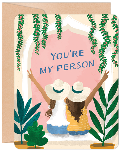 Front of a heartfelt greeting card depicting two women in hats, backs to viewer, looking out a window with lush green plants.