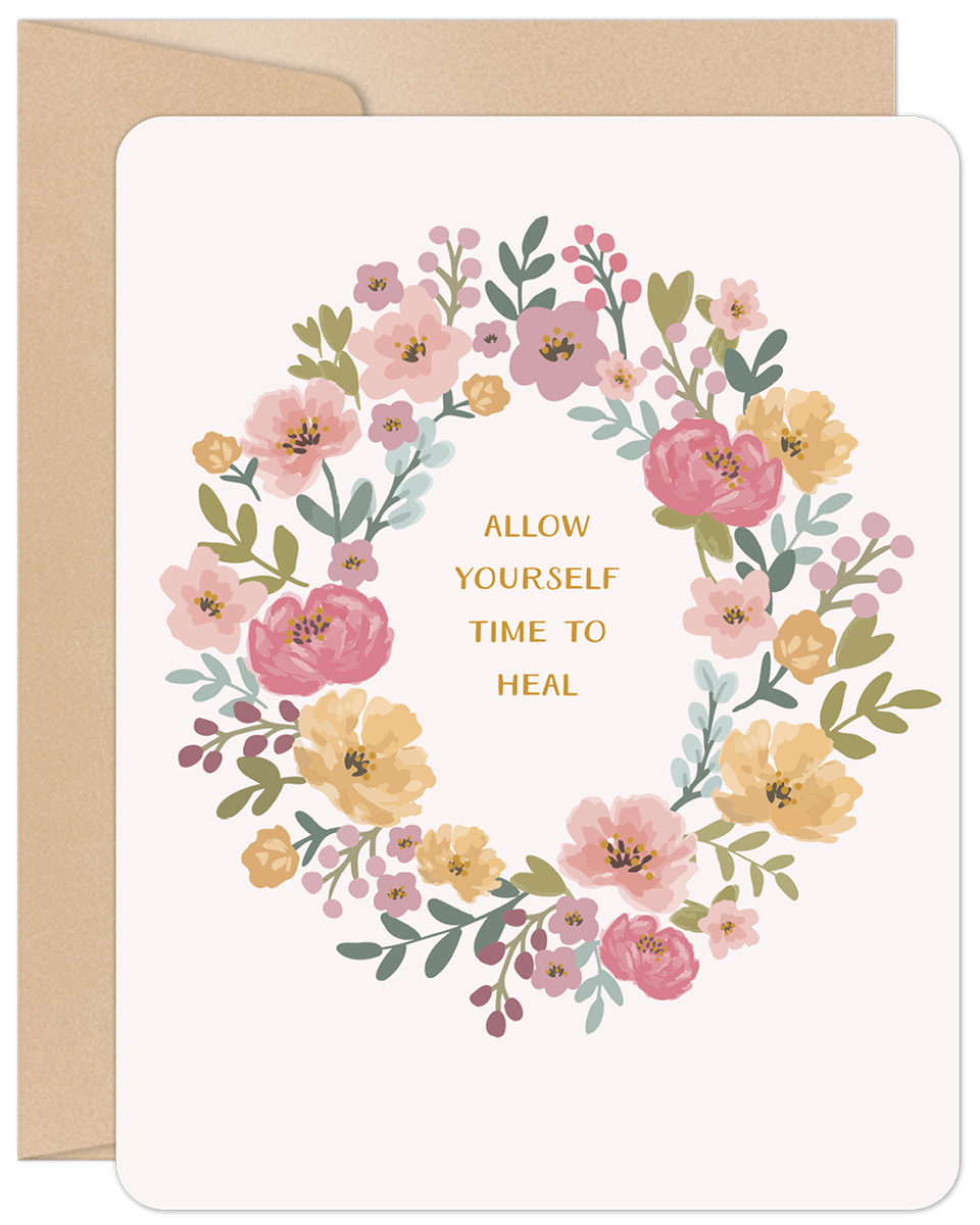 Floral wreath greeting card with pink and yellow flowers surrounding 'ALLOW YOURSELF TIME TO HEAL' message, on a kraft envelope.