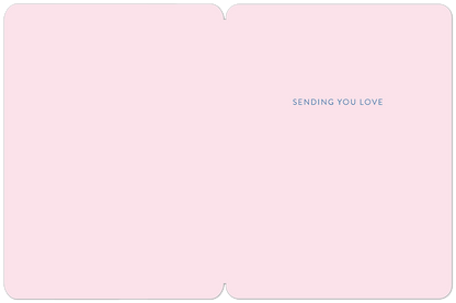 Inside a soft pink greeting card, blue text reads 'SENDING YOU LOVE' on the right panel, offering a warm, comforting message.