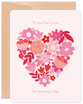 Front of a romantic floral greeting card for Valentine's Day, featuring a heart shape intricately formed by various pink, red, and white flowers on a soft pink background, with the text 'To the One I Love' and 'on Valentine's Day' in elegant script. A kraft paper envelope is visible behind it.