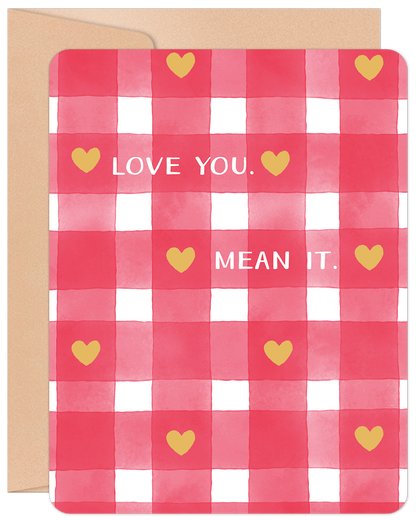 Front of a Valentine's Day card featuring a red and white watercolor gingham pattern, golden hearts, and the message "LOVE YOU. MEAN IT." in white text, all on a kraft paper envelope.