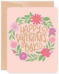 Front of a cheerful pink greeting card with a vibrant floral wreath design in pink, purple, and green, surrounding the gold text 'Happy Valentine's Day'. Perfect for a cute message.