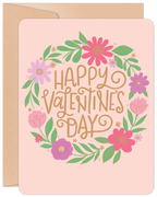 Front of a cheerful pink greeting card with a vibrant floral wreath design in pink, purple, and green, surrounding the gold text 'Happy Valentine's Day'. Perfect for a cute message.