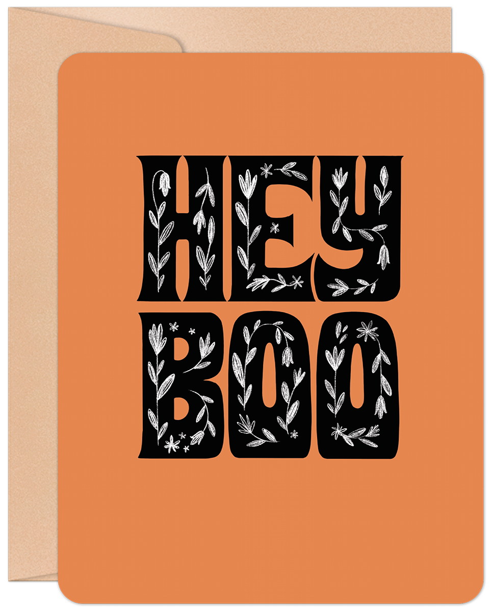 Front of a vibrant orange greeting card for Halloween, featuring decorative black text that reads 'HEY BOO' with intricate white floral and leaf patterns. A brown kraft envelope is partially visible. Ideal for sending cute spooky season wishes to friends.