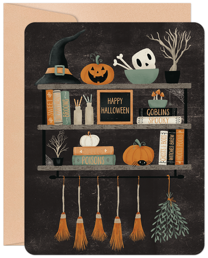 Front of a charming Halloween greeting card featuring a witch's hat, carved pumpkins, a skull, and magic books on rustic shelves.