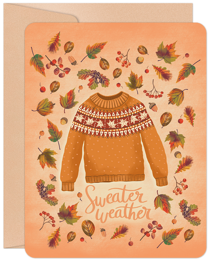 Front of a cozy fall greeting card with an orange sweater, fair isle pattern, surrounded by colorful autumn leaves, acorns, and berries. Text says 'Sweater weather'.