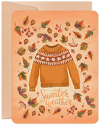 Front of a vibrant Halloween greeting card featuring an illustration of a cozy autumnal sweater, surrounded by colorful fall leaves, acorns, and berries, set against a warm orange background with 'Sweater weather' text.