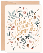 Front of a heartfelt Thanksgiving greeting card with 'Gratitude Changes Everything' in elegant calligraphy, surrounded by an autumn wreath of botanical leaves, acorns, and berries, presented with a neutral kraft envelope.