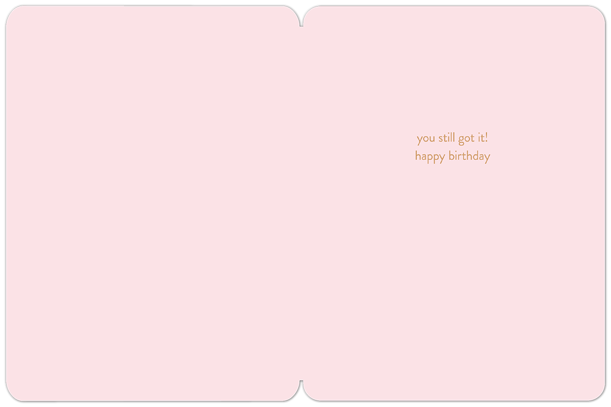 Open view of a light pink interior of a playful birthday card, showing a subtle message in elegant gold script: 'you still got it! happy birthday' with ample space for a personal handwritten note.